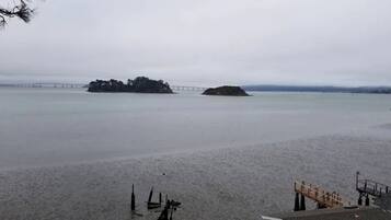A beach with a wooden pier and a bridge in the background.