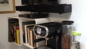 A kitchen with a coffee maker, two cups of coffee, a jar of coffee beans, a bottle of water, and a croissant on a wooden table. - Charming, private studio (Paris)