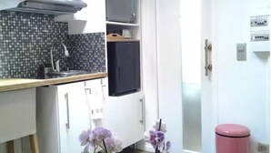 A kitchen with white cabinets, a black refrigerator, a tiled backsplash, and a pink trash bin. - Charming, private studio (Paris)