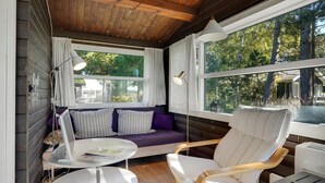 L’intérieur d’un chalet accueillant, avec un plafond en bois, un canapé agrémenté de coussins à rayures, un fauteuil blanc et une petite table.