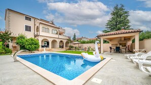A swimming pool with a swan float, a patio area with chairs, and a large tree. - Beautiful apartment in Medulin with swimming pool (Medulin)