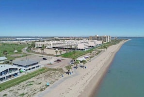 Un hotel frente al mar con varias construcciones, un estacionamiento y una playa.