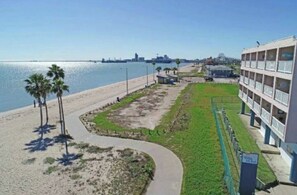 A beachfront hotel with a curved pathway leading to the beach, a grassy area, and a building with balconies.