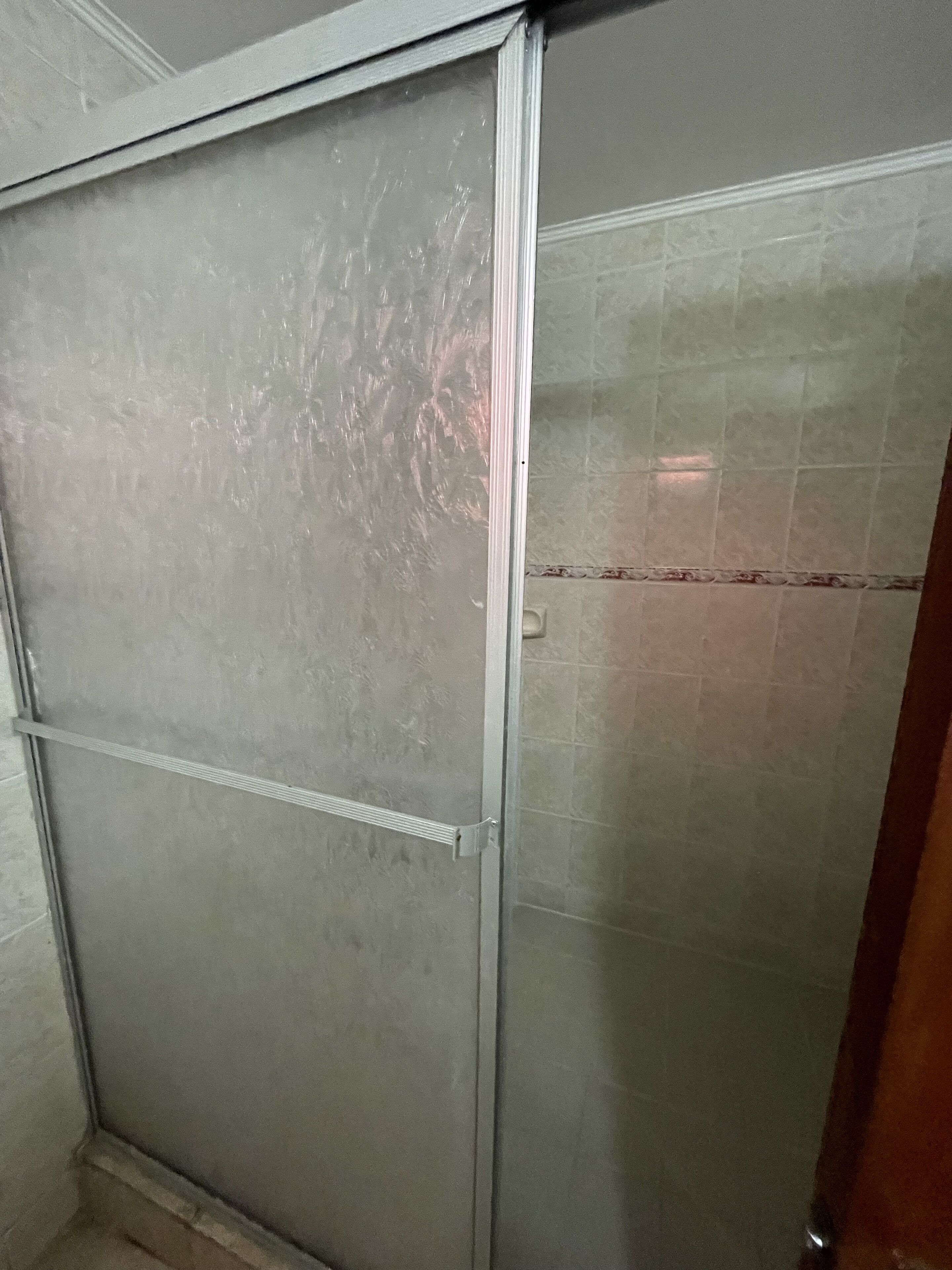 Un baño con cabina de ducha de vidrio, paredes con azulejos y un picaporte visible.