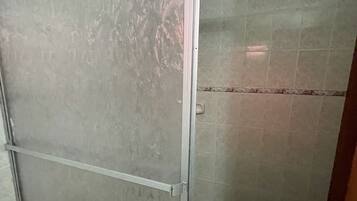 Un baño con cabina de ducha de vidrio, paredes con azulejos y un picaporte visible.