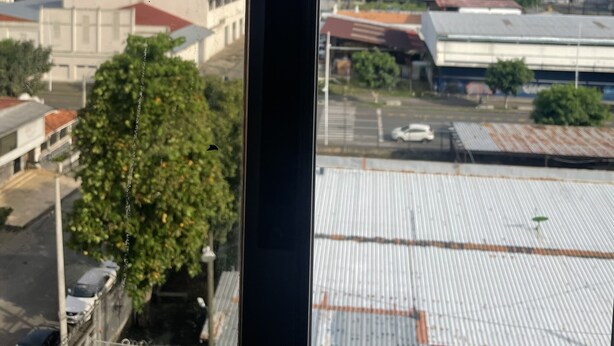 Vista a través de una ventana de un edificio de varios pisos, con una mezcla de edificios residenciales y comerciales, un estacionamiento y un cielo despejado.