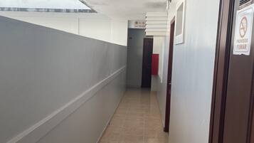 Un pasillo con suelo de baldosas, una puerta con un cartel de 'No Smoking' y una ventana a la izquierda.