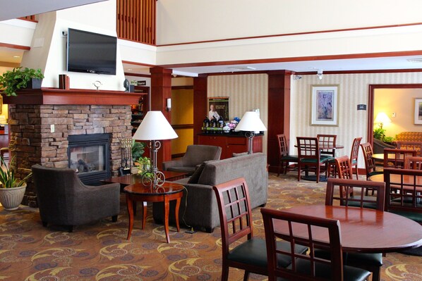 A hotel lobby with a fireplace, sofas, a dining area, and a bar.