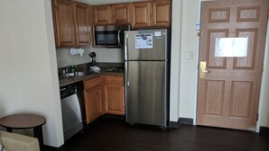 A compact kitchen with wooden cabinets, a stainless steel refrigerator, a microwave, and a dishwasher.