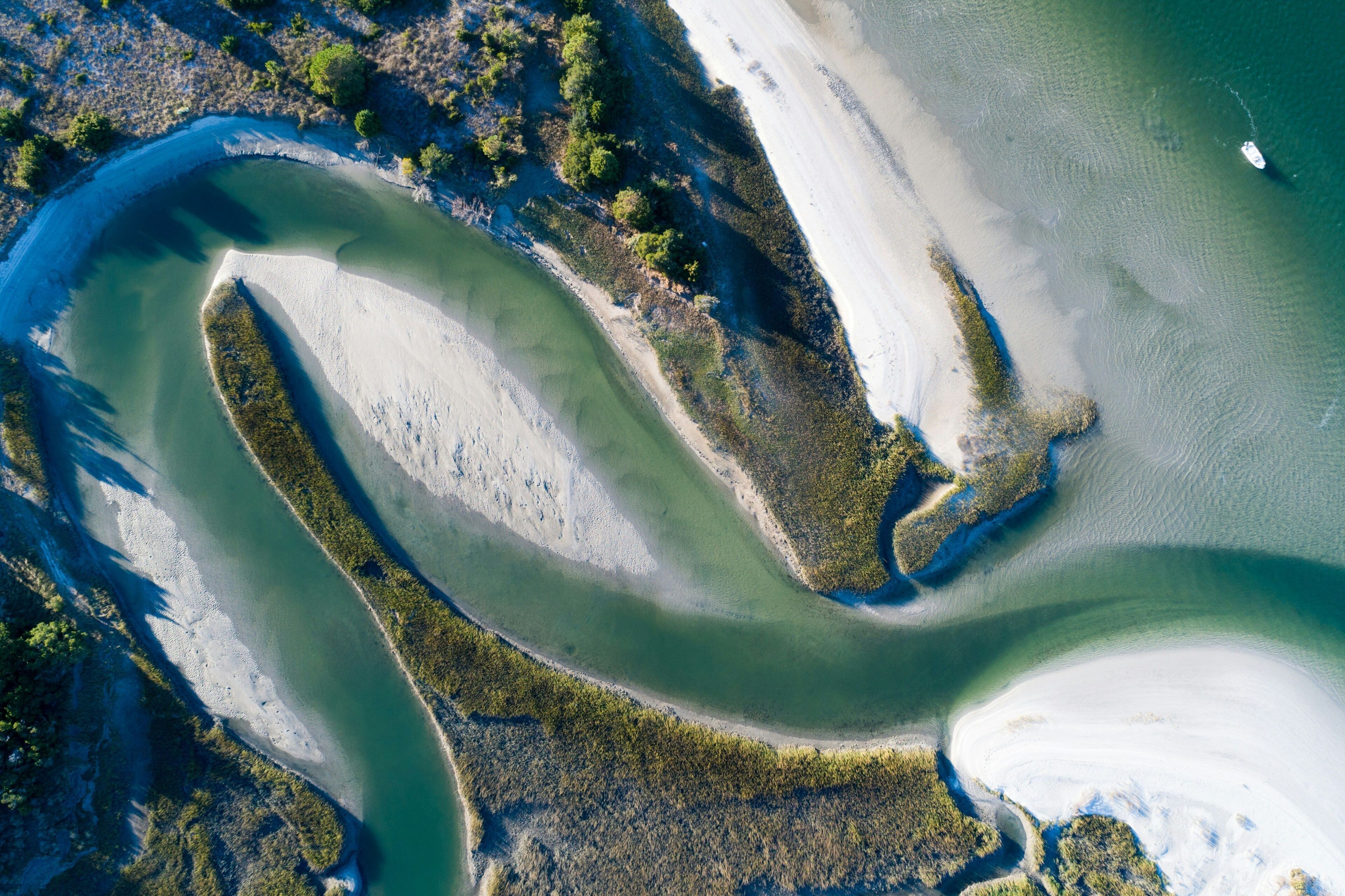 An aerial view of a coastal area with a winding river, sandy beaches, and dense vegetation.