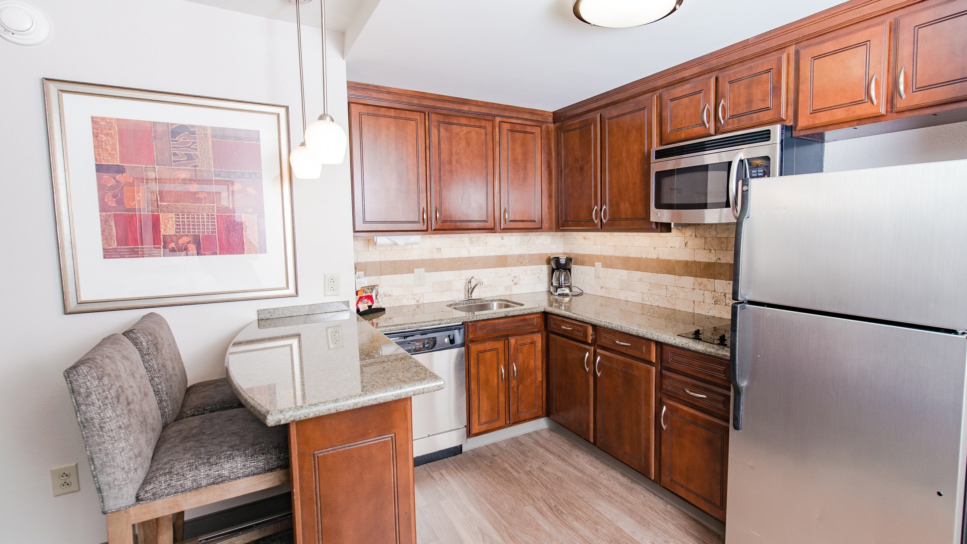 Una cocina compacta con armarios de madera, un refrigerador de acero inoxidable, un microondas y un lavavajillas.