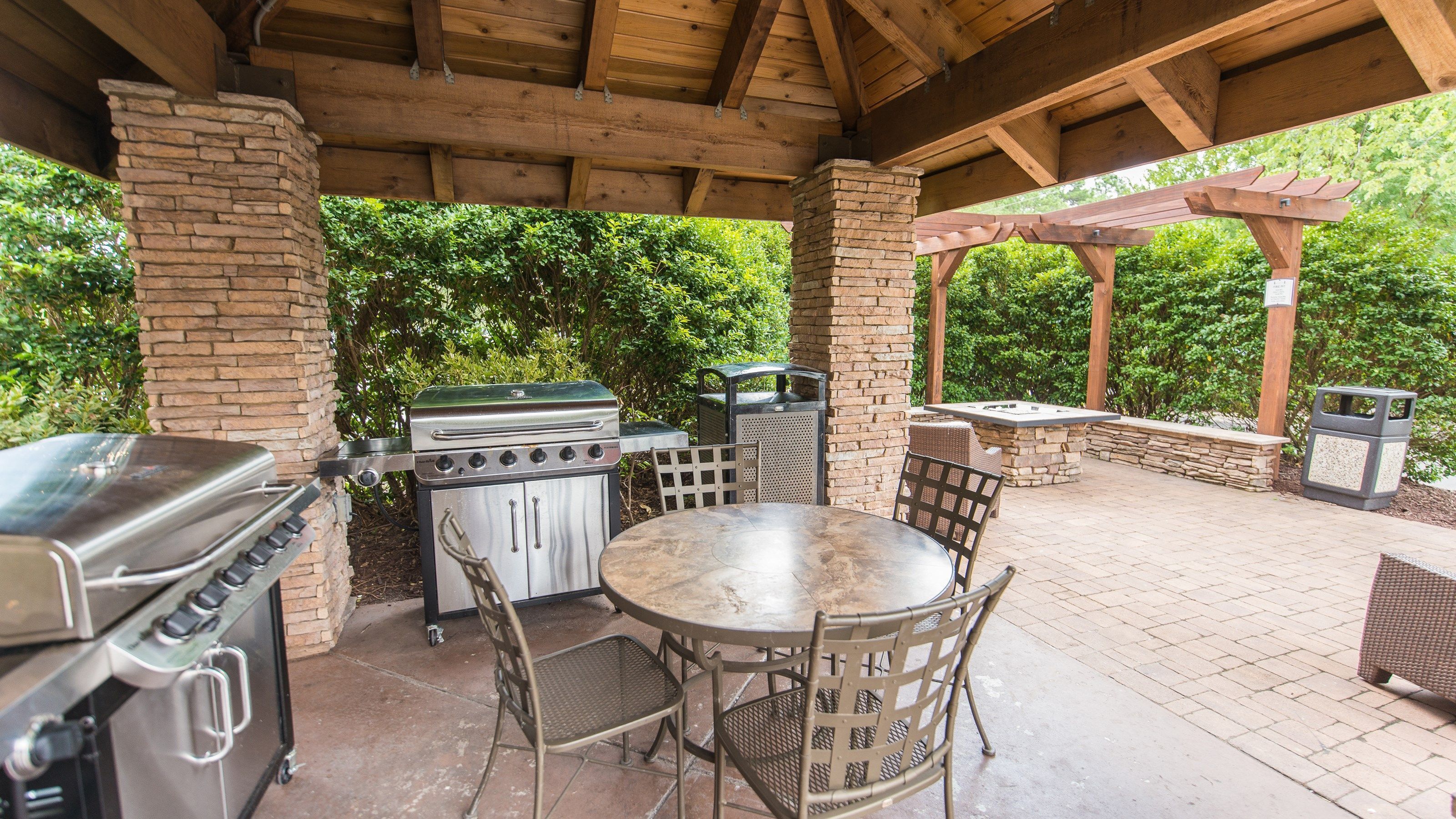 Eine Terrasse im Freien mit Grill, Tisch, Stühlen und einer Steinmauer.