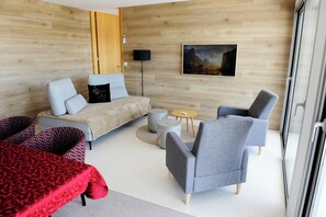 Een moderne kamer met een bank, fauteuils, een klein rond tafeltje en een schilderij aan de wand.