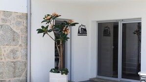 A building with a stone facade, a potted plant with yellow flowers, and a sign with a mountain and house illustration.