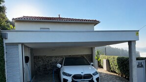 A white car parked in a covered garage with a stone wall and a tiled roof. - Casa da Montanha_Grupo Casas Vale do Lima (Arcos de Valdevez)