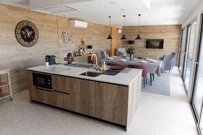 A modern kitchen with a central island, built-in appliances, and a dining area with a table set for four. - Casa da Montanha_Grupo Casas Vale do Lima (Arcos de Valdevez)