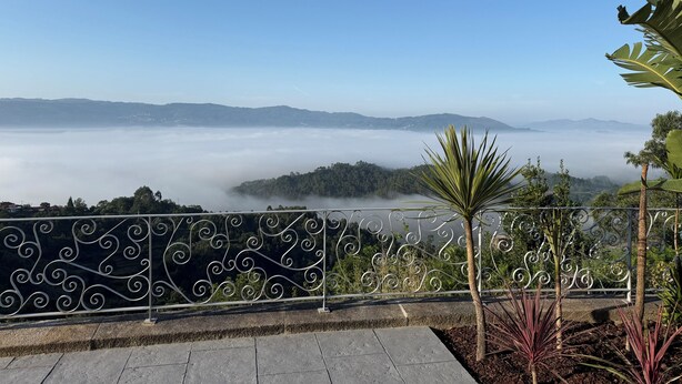 Un balcon doté d’une balustrade en métal, offrant une vue sur un paysage montagneux avec un lac et de la brume.