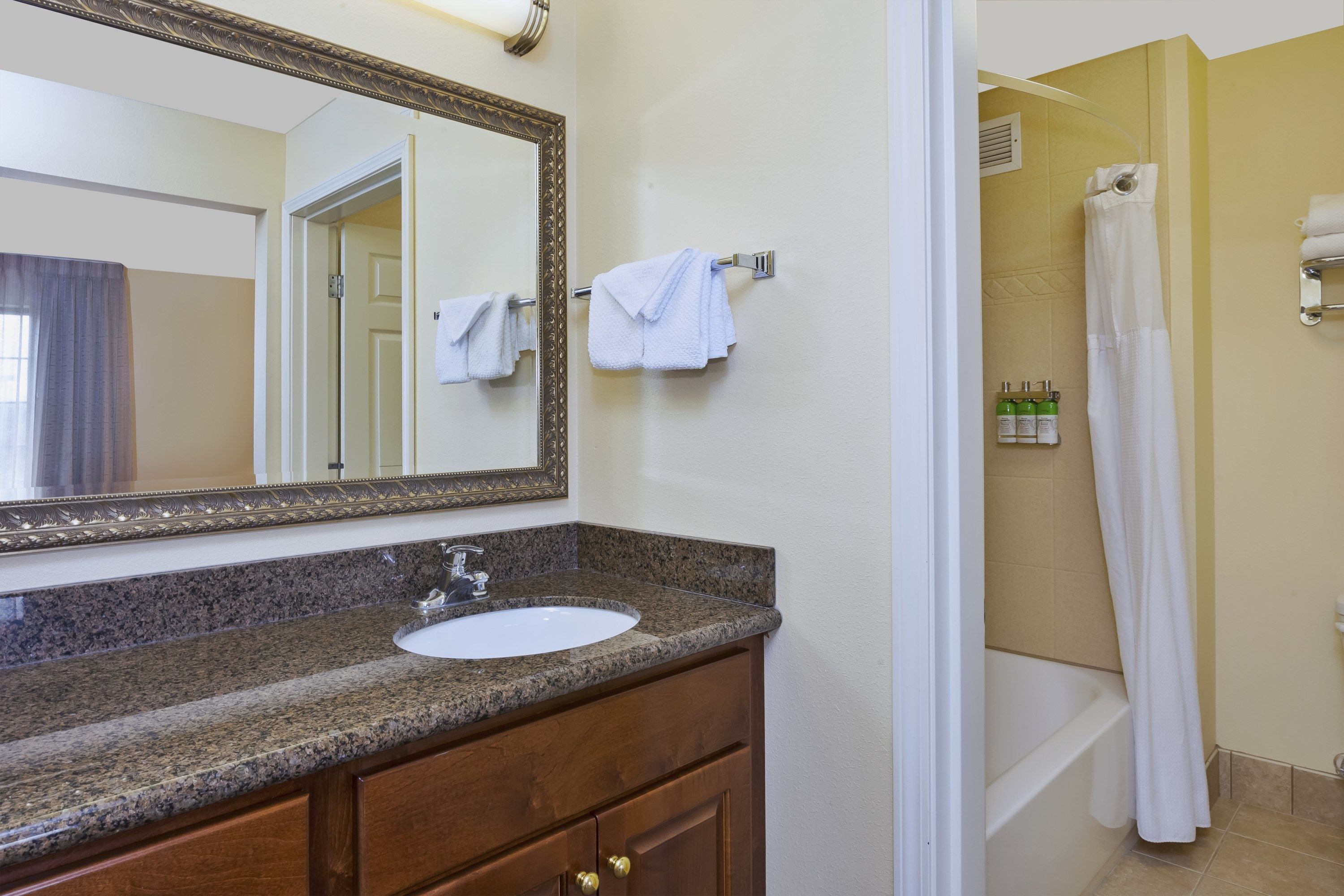 Une salle de bain avec un lavabo doté d’un plan de travail en granit, un miroir et un espace douche.