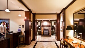 A hotel lobby with a reception desk, a stone fireplace, and a dining area with a wooden table and chairs.