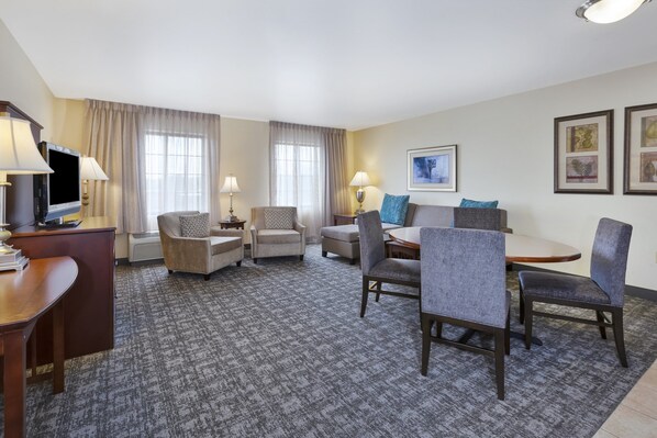 Habitación de hotel con televisión de pantalla plana, escritorio con lámpara, dos sillones, un sofá, mesa de comedor con sillas y suelo alfombrado.