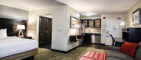 A hotel room with a bed, a sofa, a desk, a kitchenette, and a bathroom.