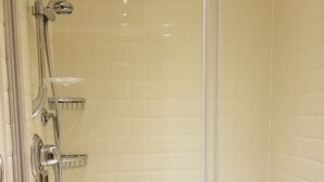 A glass-enclosed shower with a handheld showerhead, a wall-mounted faucet, and a handheld showerhead.