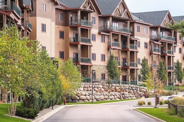 A multi-story hotel with balconies, stone walls, and a landscaped driveway.