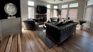 A spacious living room with a fireplace, comfortable seating, a flat-screen TV, and large windows with blinds. - Luxury 3BR Home, Comfy 🛌, WiFi, Quiet, Near (Boise)