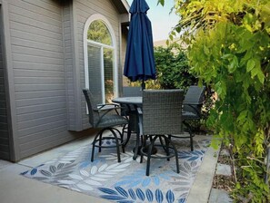 A patio with a table and four chairs, a blue umbrella, and a patterned rug. - Luxury 3BR Home, Comfy 🛌, WiFi, Quiet, Near (Boise)