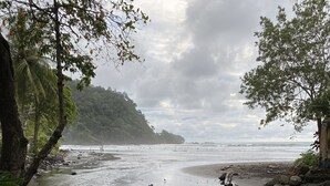 A beach with calm waters, surrounded by lush greenery and rocky outcrops. - Brand New! Jaco Beach outside the back gate! (Jaco)