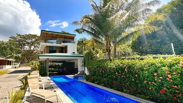 A modern house with a swimming pool, surrounded by lush greenery and palm trees. - Brand New! Jaco Beach outside the back gate! (Jaco)