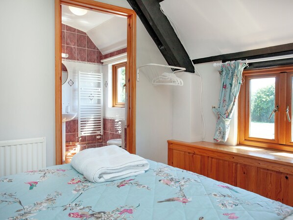 A bedroom with a bed, wooden wardrobe, a window with curtains, a bathroom with a shower, and a tiled wall.