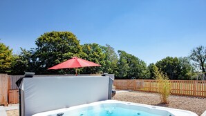 Un bain à remous avec un parasol rouge, entouré d’une clôture en bois et d’arbres.
