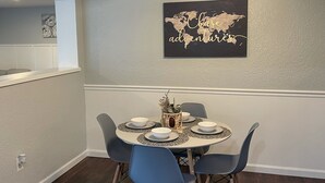 Uma sala de jantar com uma mesa redonda, seis cadeiras, um ventilador de teto e uma obra de arte com um mapa-múndi na parede.