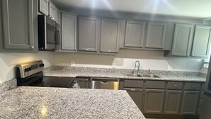 Cozinha com bancadas de granito, eletrodomésticos de aço inoxidável e armários cinzas.