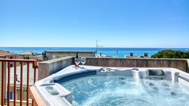Een jacuzzi met een digitaal bedieningspaneel, een glas en een fles, met uitzicht op de kust, gebouwen en de zee.