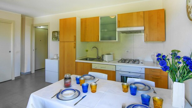A compact kitchen with wooden cabinets, a white countertop, and a dining area set for four with blue and yellow glassware. - Beautiful apartment in Lavagna with WiFi (Lavagna)