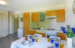 A compact kitchen with wooden cabinets, a white countertop, and a dining area set for four with blue and yellow glassware.