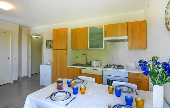 A compact kitchen with wooden cabinets, a white countertop, and a dining area set for four with blue and yellow glassware. - Beautiful apartment in Lavagna with WiFi (Lavagna)