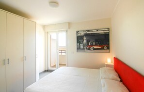 A bedroom with a bed, a wardrobe, a door leading to a balcony, and a wall-mounted picture of a vintage car.