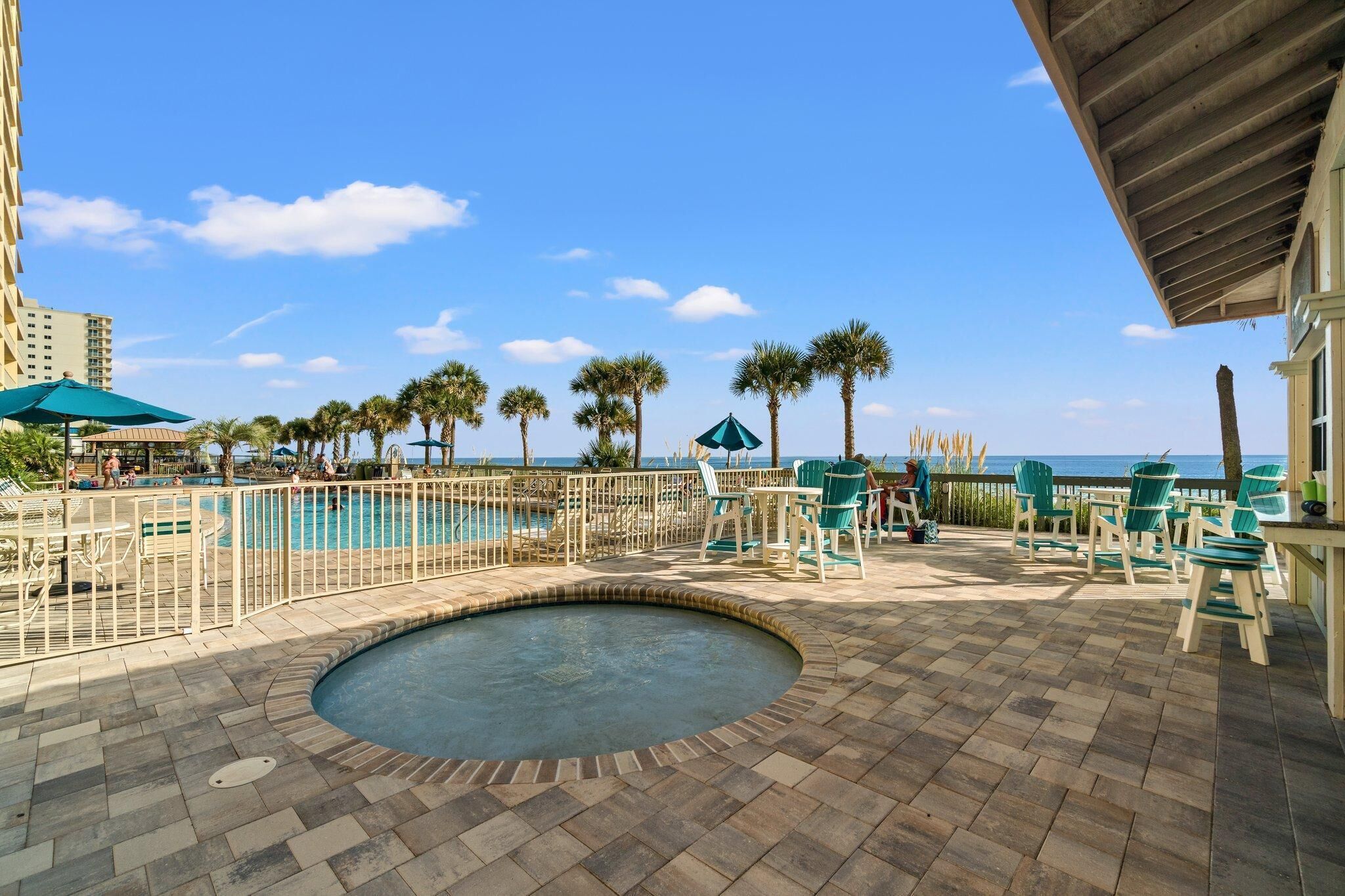 A pool area with a hot tub, lounge chairs, and palm trees.