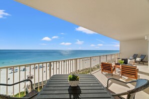 A balcony with a view of the beach and ocean, wooden furniture, and a potted plant. - Renovated, Family-Focused Gulf Crest Condo! Miles-long views of the shoreline! (Panama City Beach)