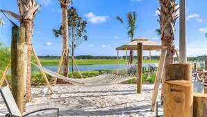 Une plage avec un hamac, des chaises en bois, une structure en bois et une vue sur l’eau.