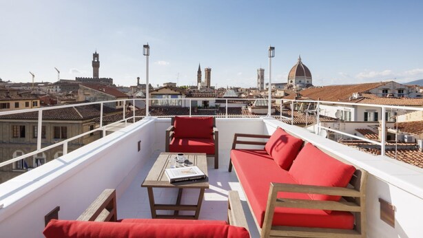 Eine Dachterrasse mit rotem Sofa, Holztisch und Blick auf historische Gebäude.