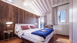 Ein Schlafzimmer mit Bett, Nachttischlampen, Schreibtisch, Spiegel und einem Fenster mit Vorhängen.