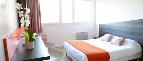A hotel room with a bed, a desk, a chair, and a window with curtains.