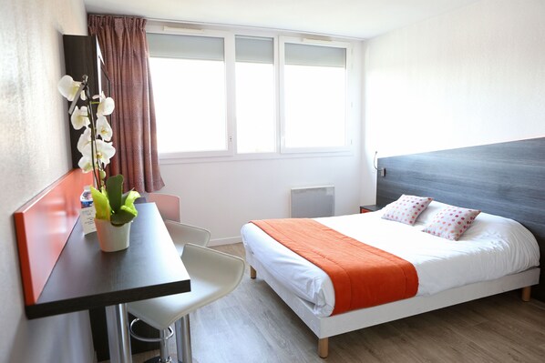 A hotel room with a bed, a desk, a chair, and a window with curtains.
