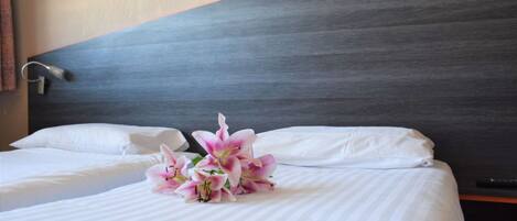 A hotel room with two beds, white linens, a dark headboard, and a bouquet of pink flowers on the bed.