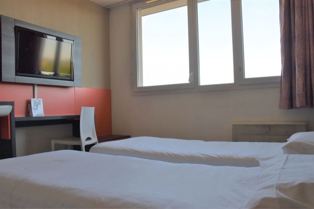 Une chambre d’hôtel avec deux lits, un bureau avec une chaise, une télévision et une fenêtre avec des rideaux.