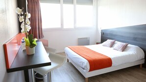 A hotel room with a bed, a desk, a chair, and a window with curtains.